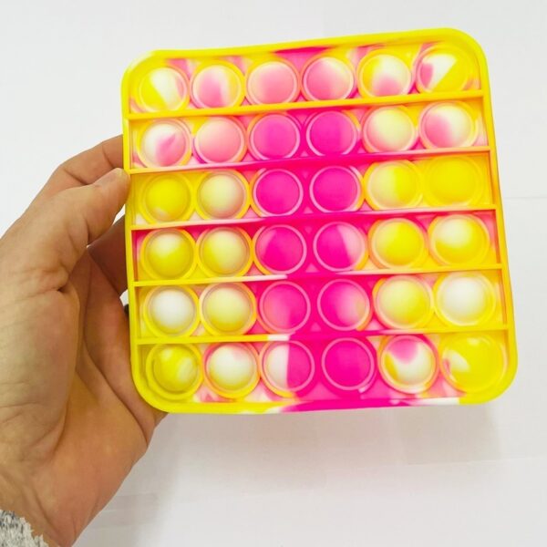 A hand holds up a yellow and pink fidget pop it square toy.